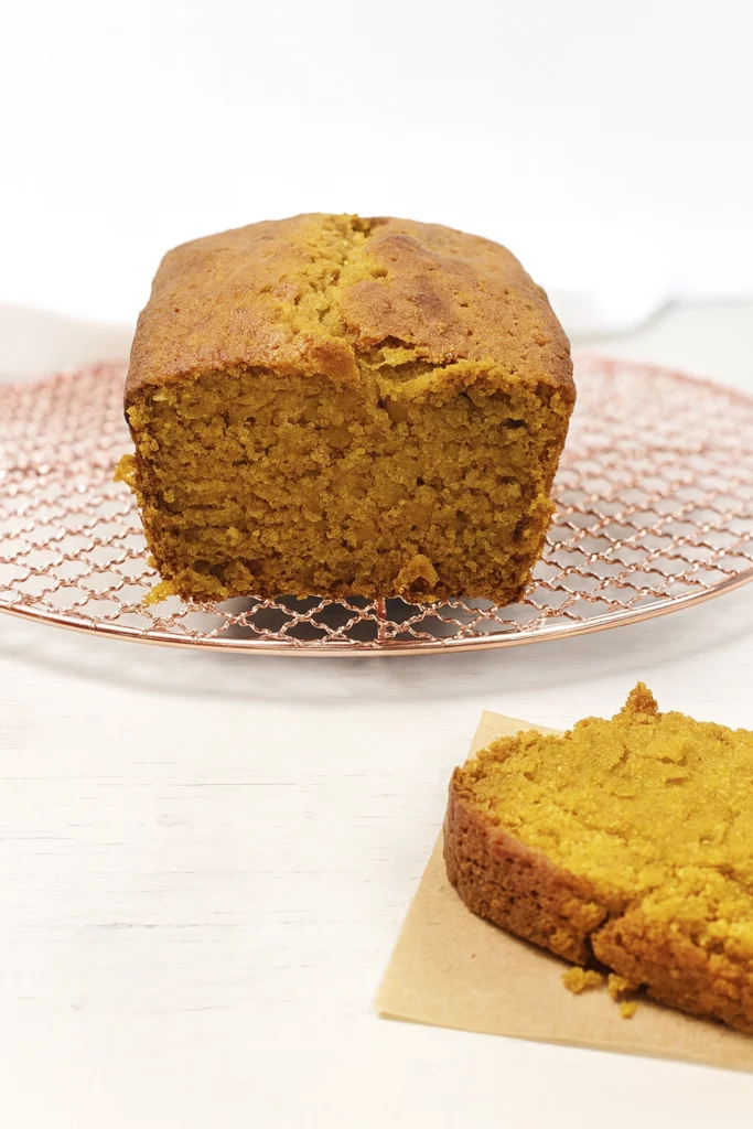 Pumpkin bread loaf on copper cooling rack with a sliced piece on parchment paper, styled for autumn food photography.