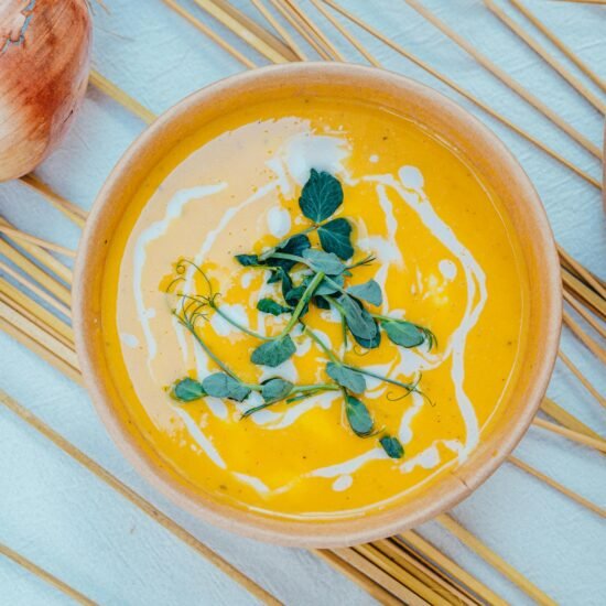 Bowl of hot soup with fresh herbs and bread on a wooden table in warm natural light.