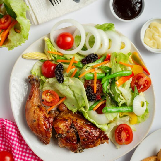 Healthy lunch plate with grilled chicken, vegetables, and salad on a wooden table.