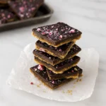 Stack of festive chocolate peppermint bark with crushed candy on parchment paper over marble.