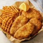 Basket of fried fish fillets and waffle fries on parchment paper