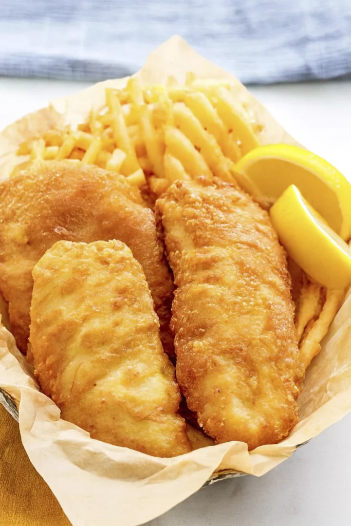 Golden fried fish fillets with waffle fries and lemon wedge in parchment-lined basket