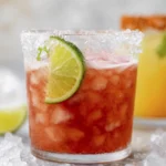 Refreshing reddish cocktail with lime and salt rim surrounded by colorful summer drinks on crushed ice.