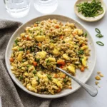 Plate of vegetable fried rice with green onions, peas, carrots, and scrambled eggs in a bright setting