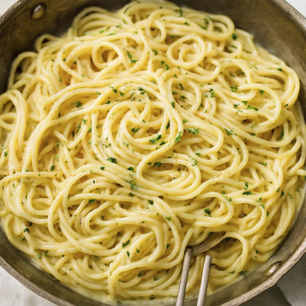 Creamy spaghetti pasta in skillet with parsley garnish and serving utensils