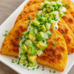 Crispy glazed chicken frying in oil with steam, garnished with sesame seeds, scallions, and lime.
