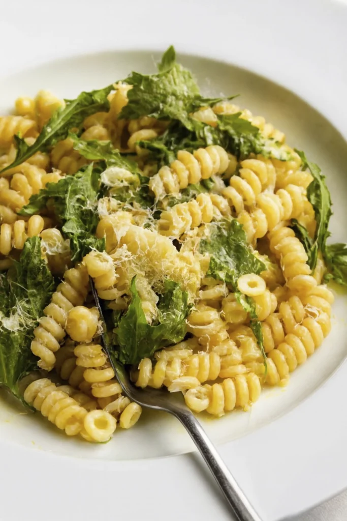 Spiral pasta with fresh herbs and Parmesan cheese, served with a fork on a white plate.