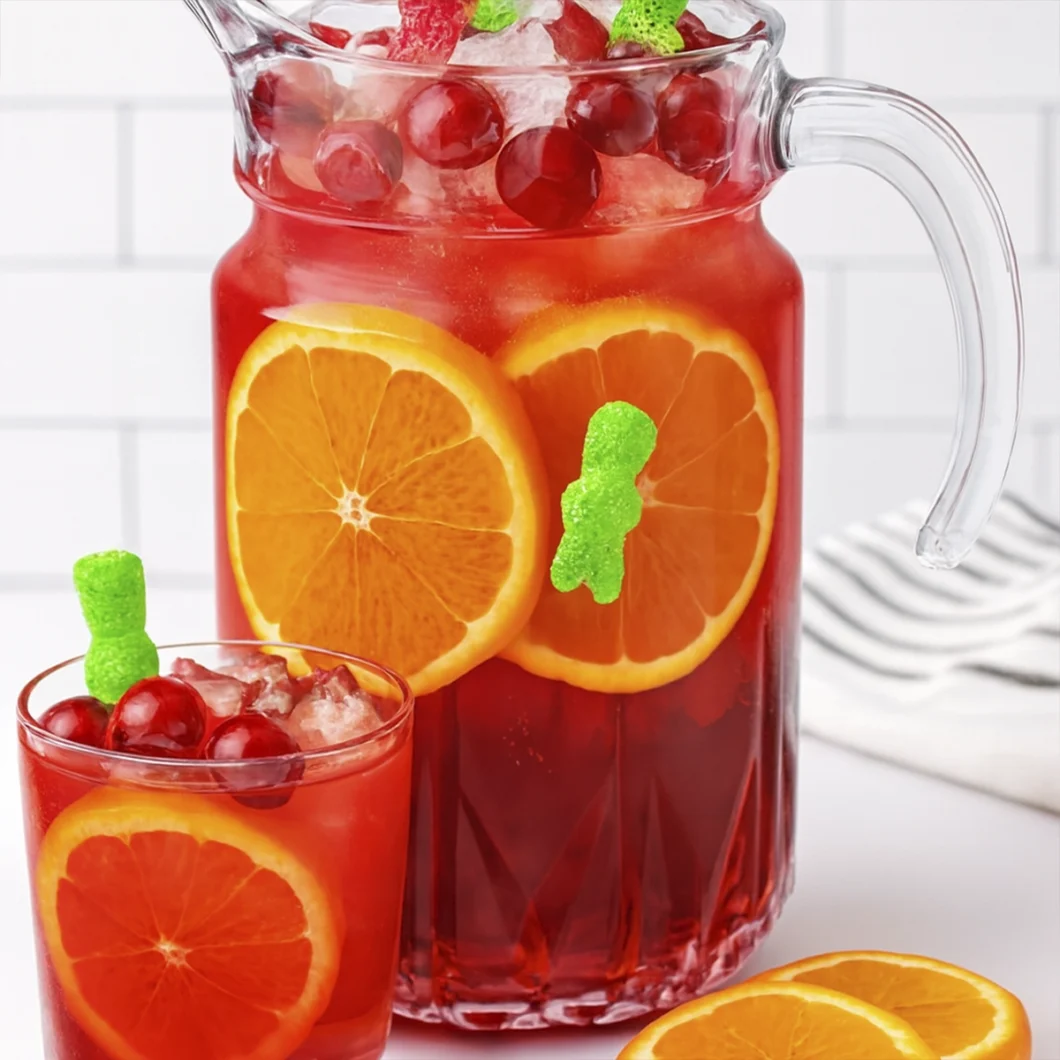Red fruit punch with orange slices, cherries, and gummy bears in a glass and pitcher.