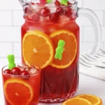 Red fruit punch with orange slices, cherries, and gummy bears in a glass and pitcher.