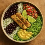 Vibrant fish burrito bowl with grilled white fish, cilantro-lime rice, black beans, avocado, pico de gallo, lettuce, and lime wedges in ceramic dish