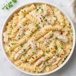 Creamy rotini pasta with shredded chicken in Parmesan sauce, garnished with herbs and pepper flakes.