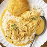 Southern-style creamy shredded chicken in yellow sauce over rice, garnished with parsley, biscuit and iced tea.
