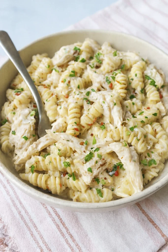 Overhead view of creamy rotini pasta with shredded chicken, parsley, and pepper in a rustic bowl.