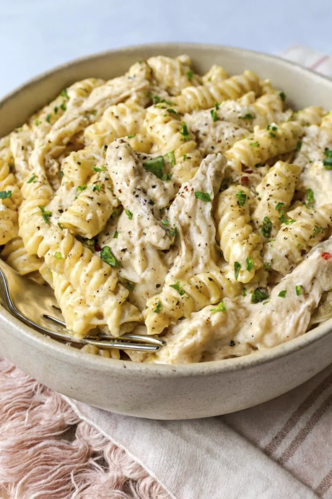 Side view of creamy rotini pasta with parmesan sauce, shredded chicken, and fresh herbs.