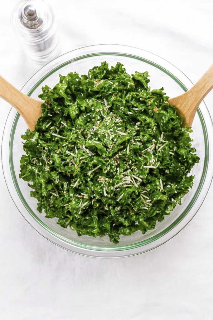 Minimalist kale salad with cheese and seeds in a glass bowl on white background.
