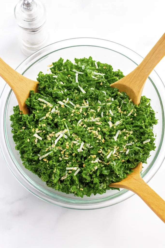 Fresh kale salad with cheese and seeds in a glass bowl with wooden servers.