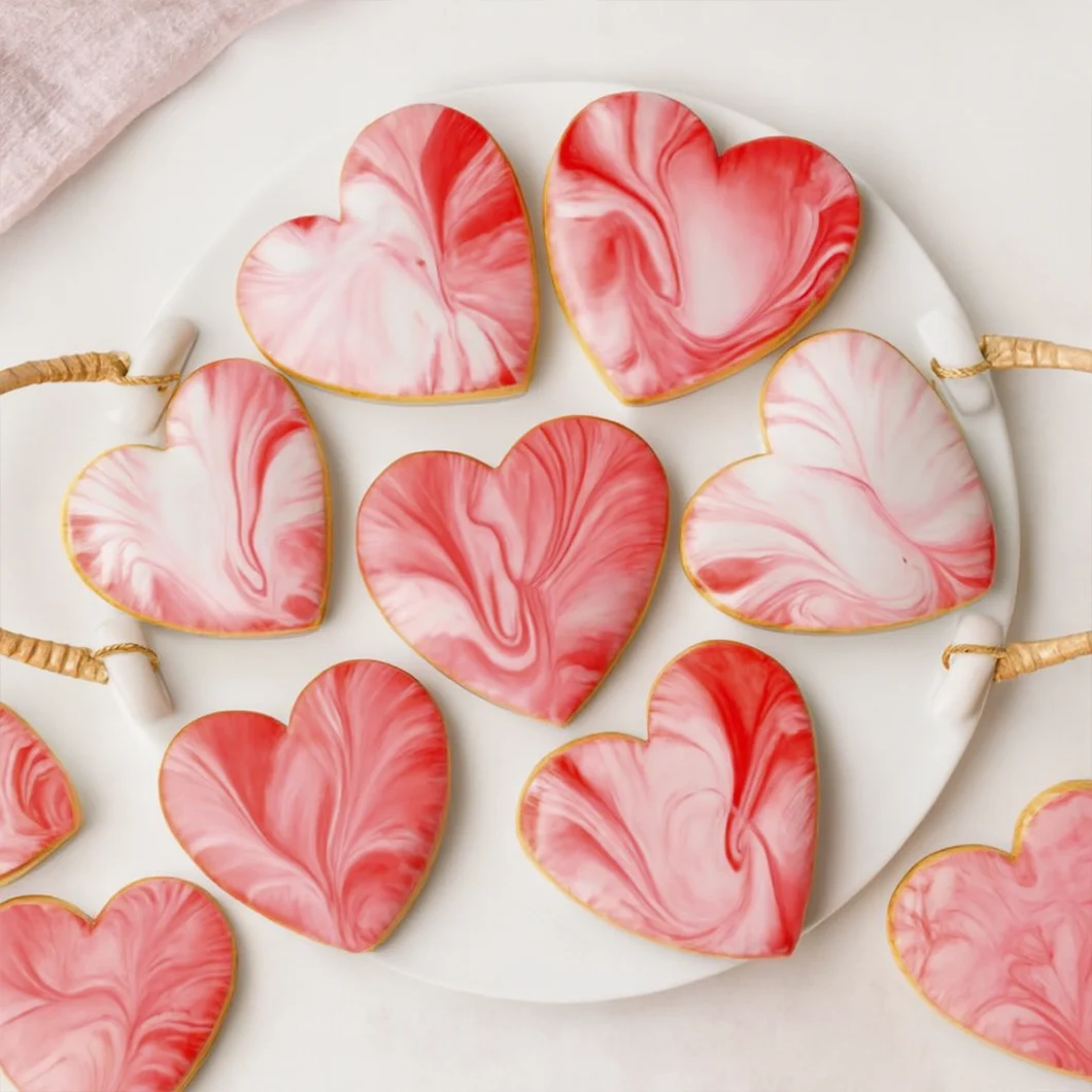 Heart-shaped cookies with pink marbled icing on a white plate with woven handles.