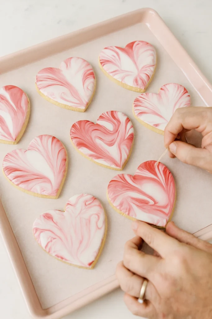 Bitten heart-shaped sugar cookie with red and white marbled icing stacked on soft background