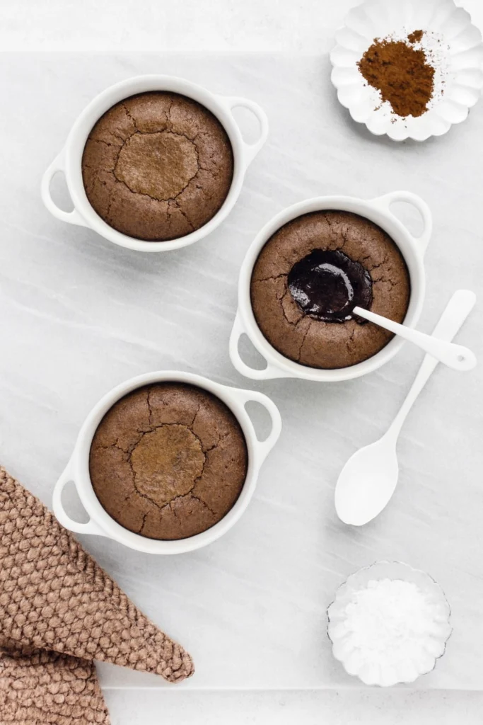 Freshly baked chocolate lava cakes in ramekins with molten centers and cocoa powder garnish.