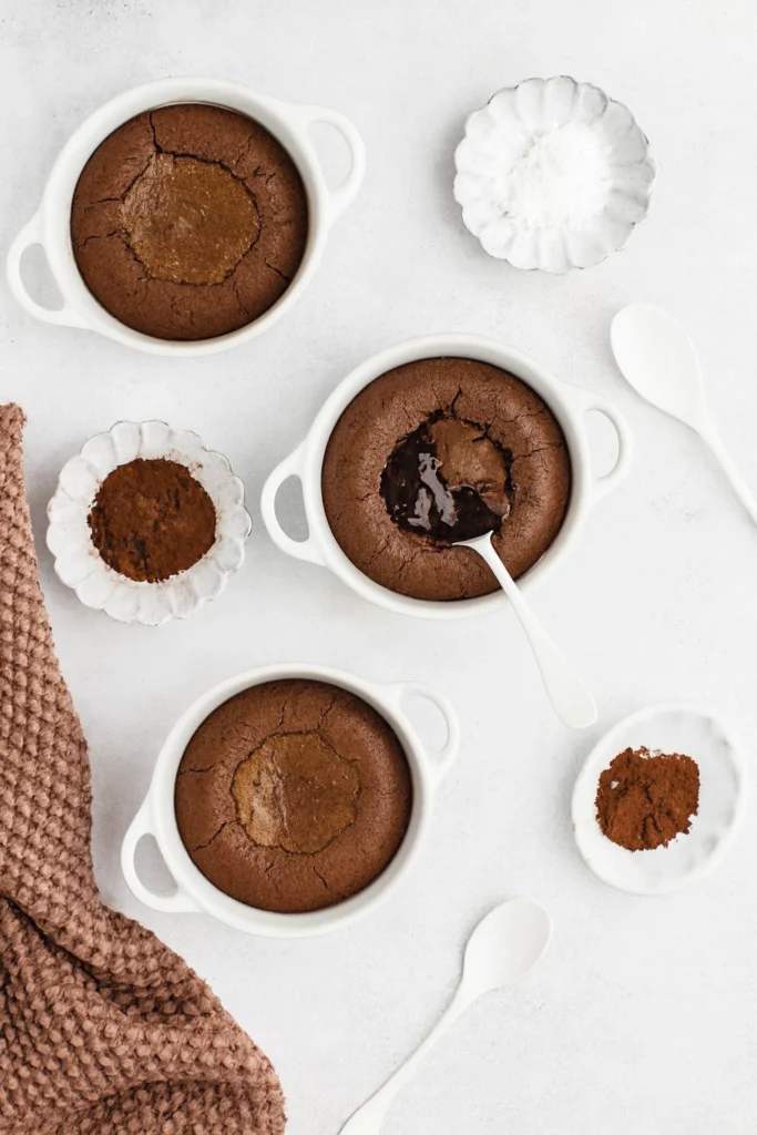 Molten chocolate lava cakes in ceramic ramekins with spoon revealing gooey center on marble.