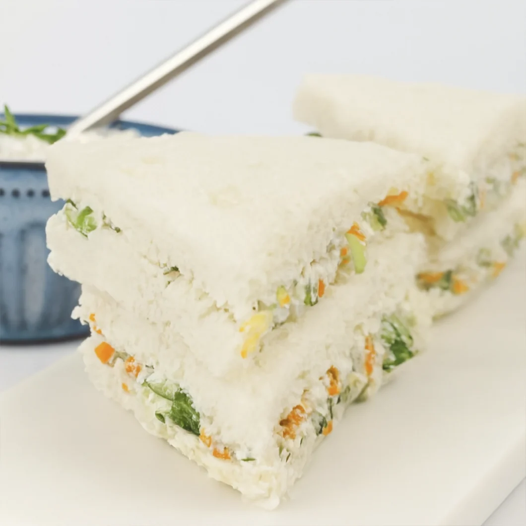 Close-up of creamy vegetable sandwiches on white bread with fresh ingredients and minimalist styling.