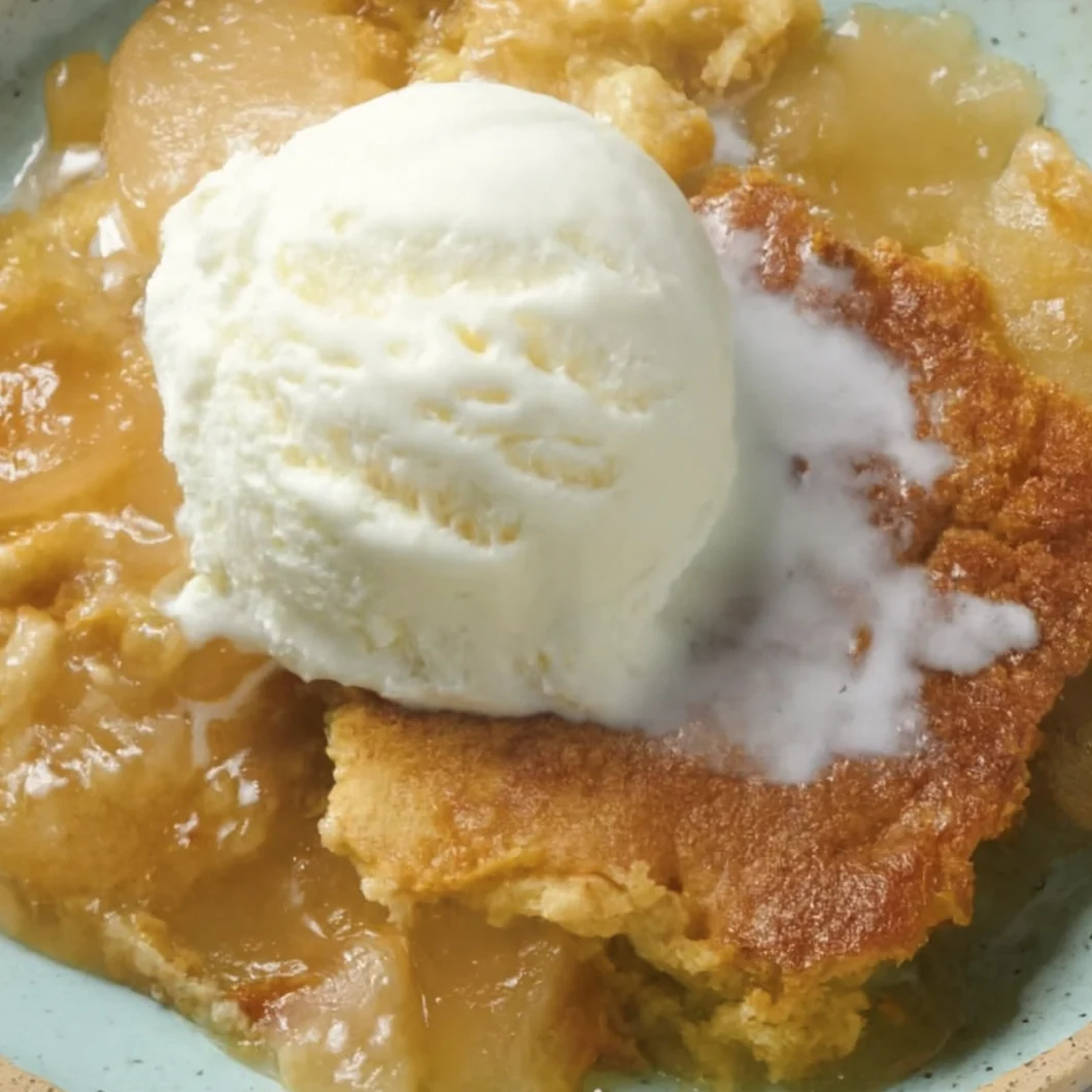 Warm apple cobbler topped with melting vanilla ice cream in a rustic ceramic bowl.