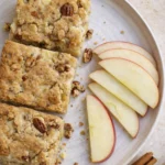 Fresh apple brownies with pecans, sliced apples, and cinnamon sticks on a rustic plate.