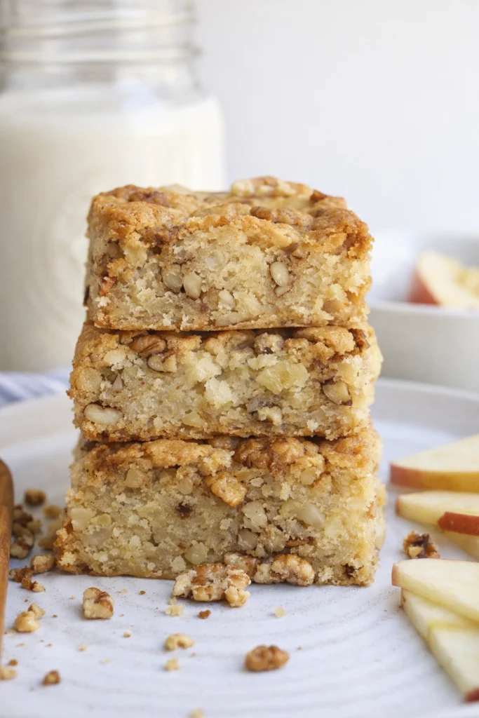 Freshly baked apple brownies cut into uniform rectangular bars with golden-brown crust, visible apple chunks and pecans, arranged neatly on parchment paper.