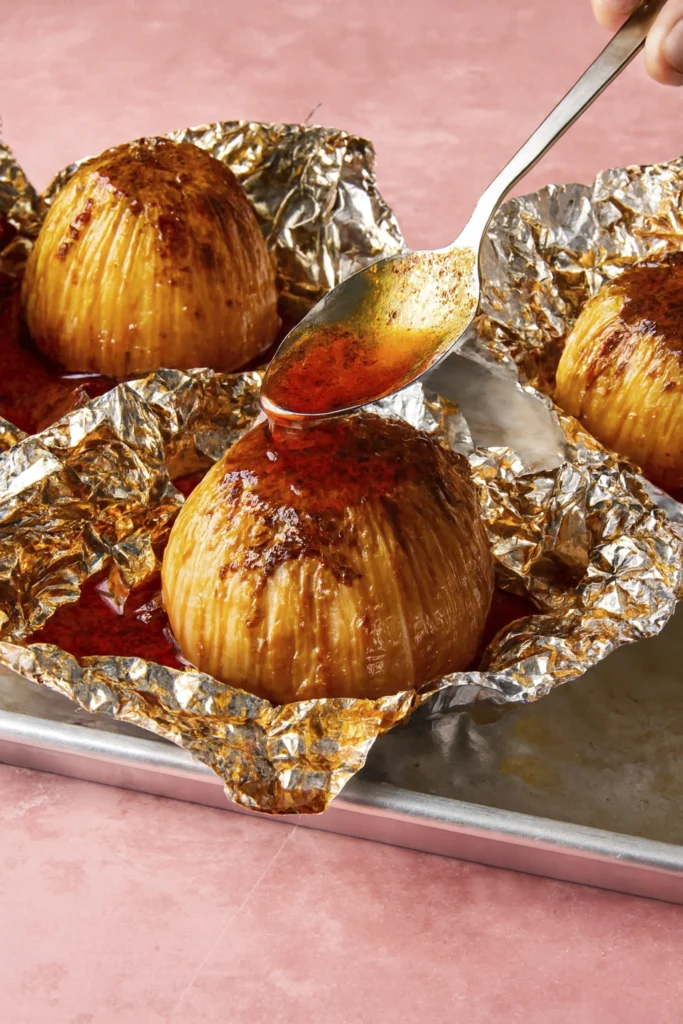 Four roasted onions in foil with sauce drizzle on baking tray