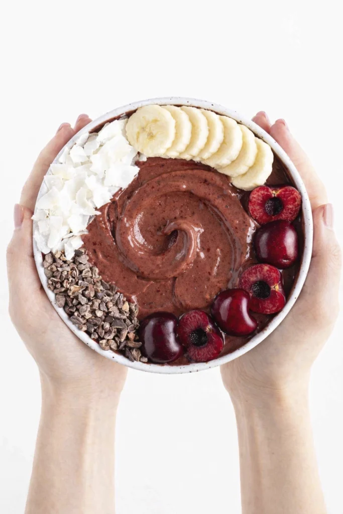 Smoothie bowl with bananas, cherries, cacao nibs, and coconut flakes.