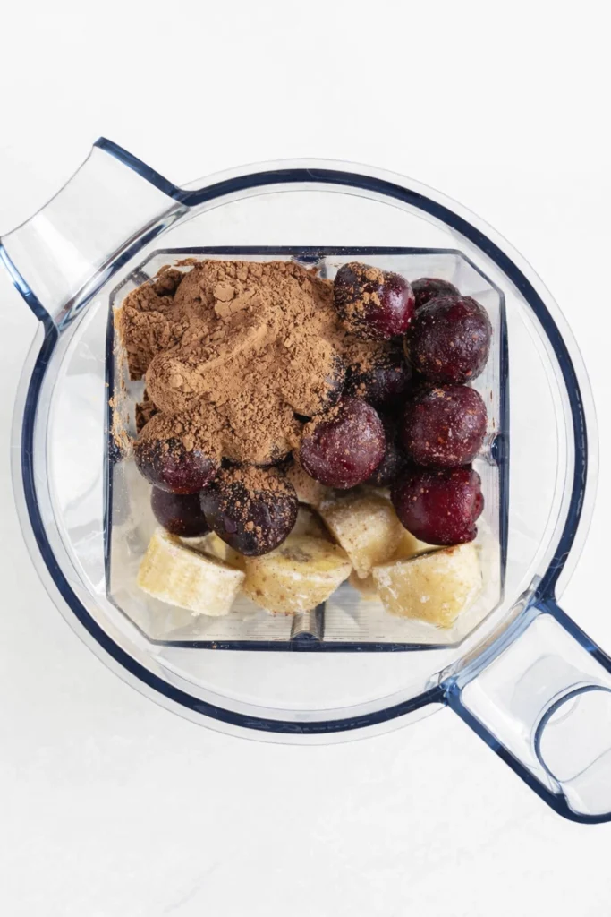 Blender filled with frozen bananas, cherries, and cocoa powder.