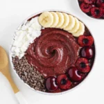 Healthy smoothie bowl with cherries, bananas, coconut flakes, and cacao nibs on a white background