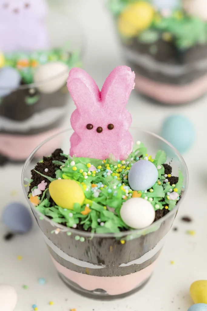 Easter dirt cups with pink and white cream, cookie crumbs, green coconut grass, sprinkles, candy eggs, and marshmallow bunny Peeps.