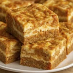 Moist carrot cake bars topped with cream cheese frosting and spiced with cinnamon, cut into neat squares.