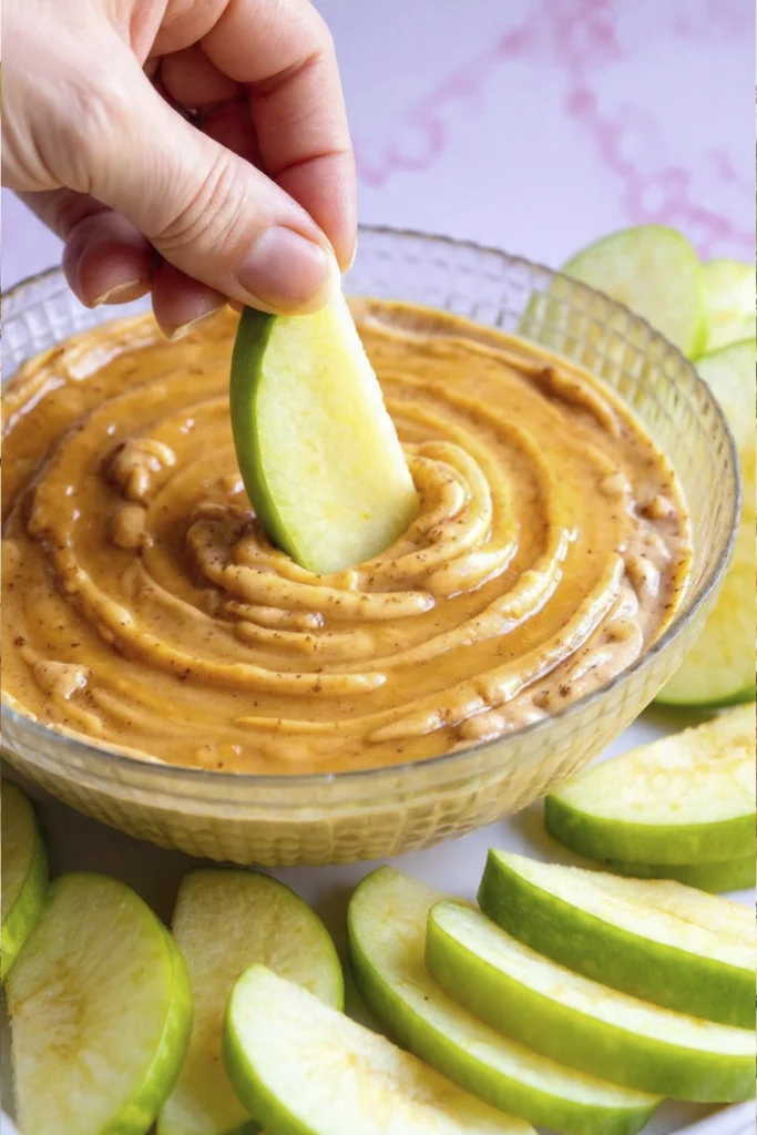 Hand dipping a fresh green apple slice into creamy Greek Yogurt Apple Dip