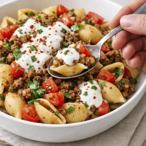 Turkish pasta recipe served in a rustic ceramic bowl with spiced ground beef, garlic yogurt sauce, cherry tomatoes, fresh parsley, and a drizzle of red pepper butter on a wooden table